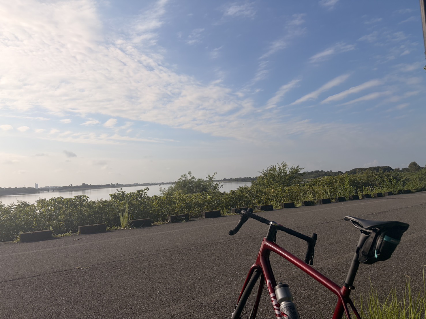 渡良瀬遊水地の広い平坦路に停めた赤いロードバイクと、朝の水面と空
