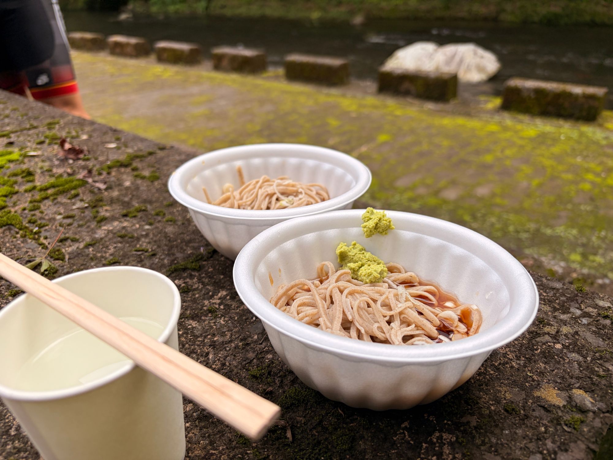 川沿いの石垣に置いた二つのそばの器。手前の器にはわさびが載っている