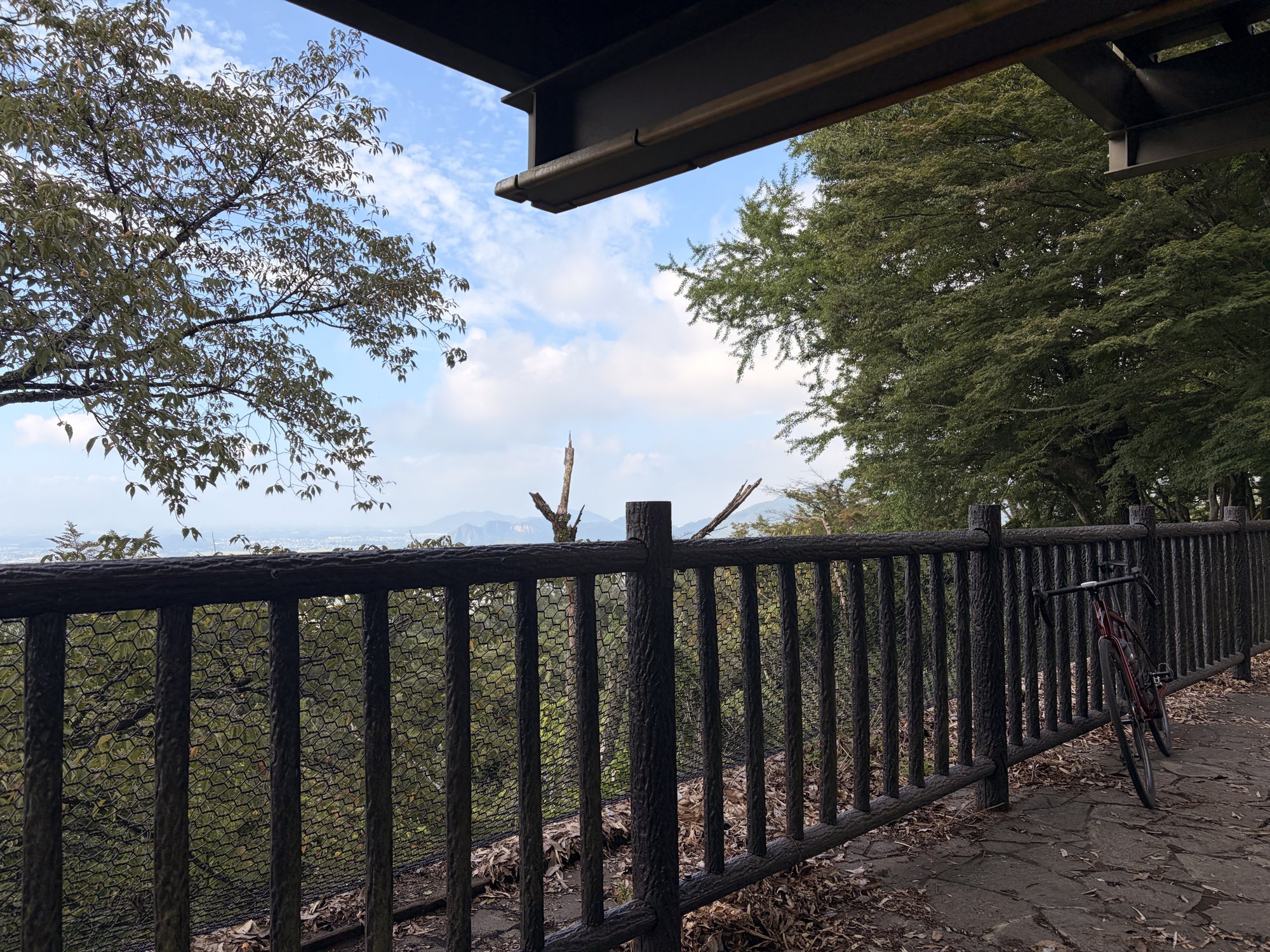 展望台の柵の向こうに広がる青空と遠くの山並み。柵に赤いロードバイクが立てかけてある